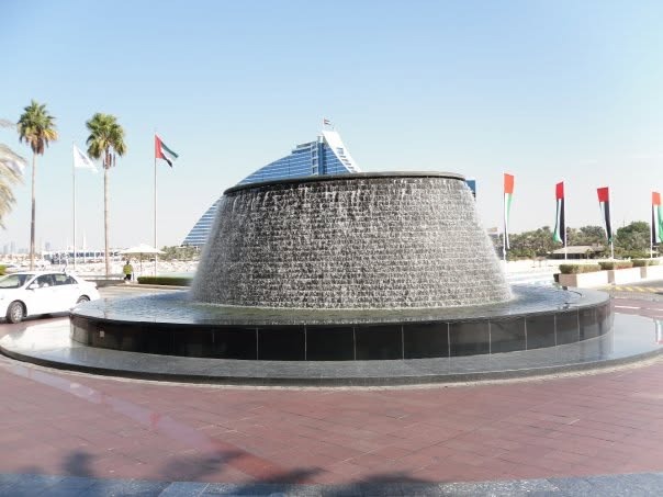 A giant round waterfall fountain at the entrance, with the Jumeirah Beach Hotel behind