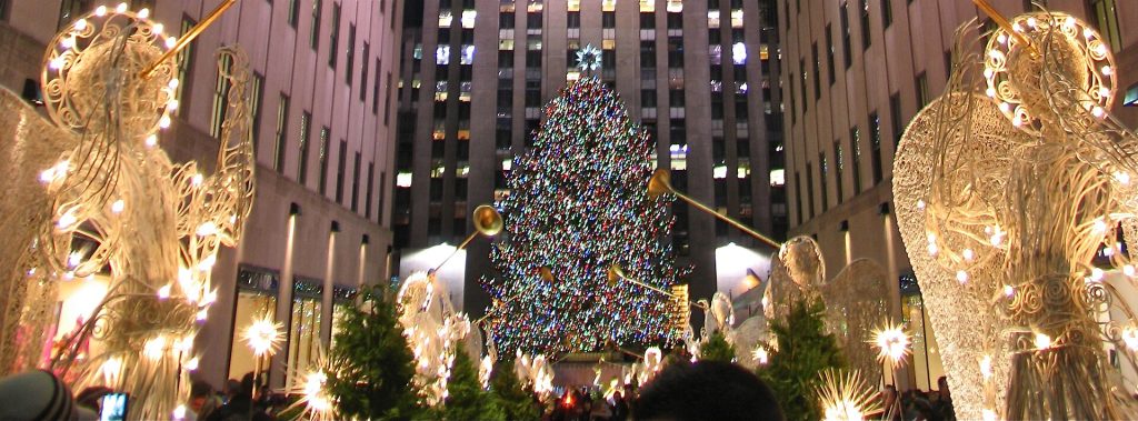 The Rockefeller Center Christmas tree lit up behind golden angel decorations
