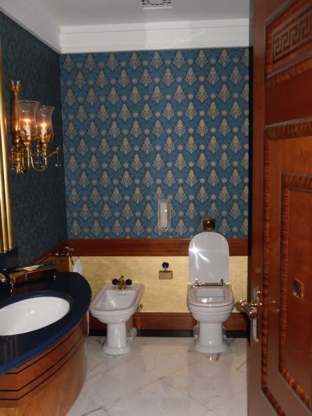 A powder room with blue damask wallpaper, gold sconces and a curved vanity