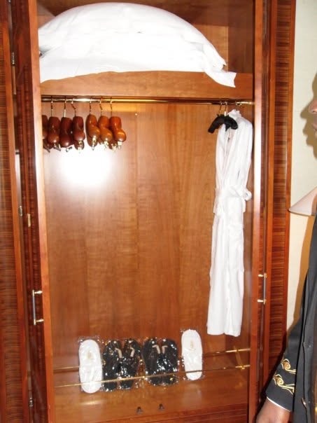 A wood wardrobe with a white robe, slippers and wooden hangers